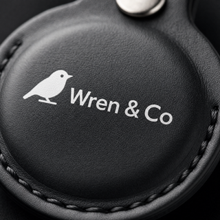 Close-up of white logo printed on black vegan leather AirTag holder