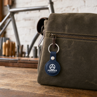 Blue leather AirTag holder with company logo clipped to a workshop bag