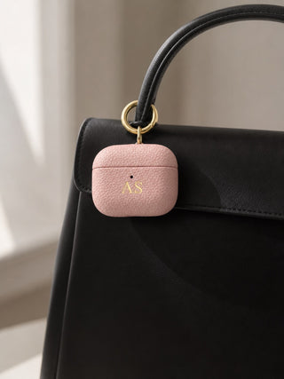 Pink personalised leather AirPods case clipped to a black handbag