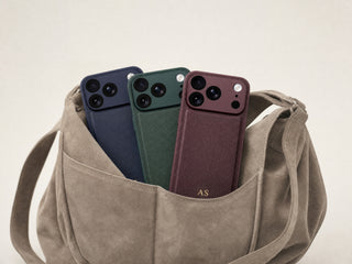 Three personalised leather iPhone cases in burgundy, green and navy tucked into a suede bag pocket